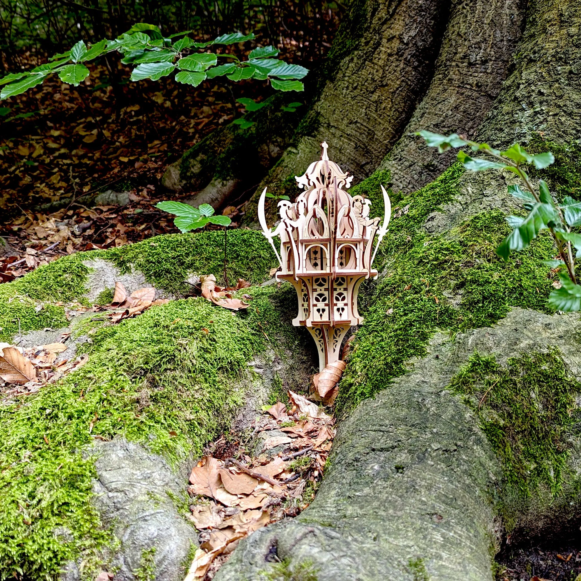 Ground level shot of a laser cut plywood fairy elven outpost model with crescent details positioned next to a big tree.