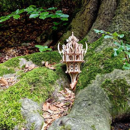 Ground level shot of a laser cut plywood fairy elven outpost model with crescent details positioned next to a big tree.