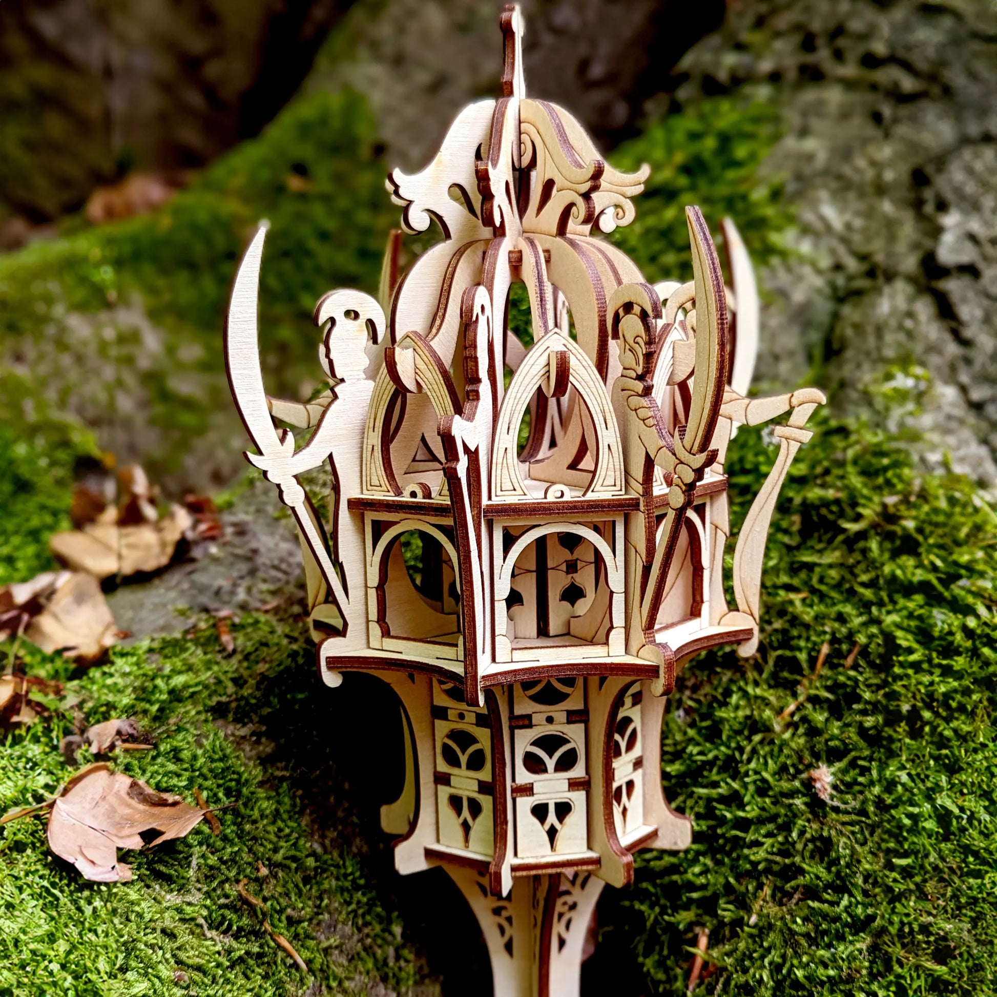 Macro shot of a laser cut plywood gothic elven tower model showing precise dark burnt edges on moss covered wood background.