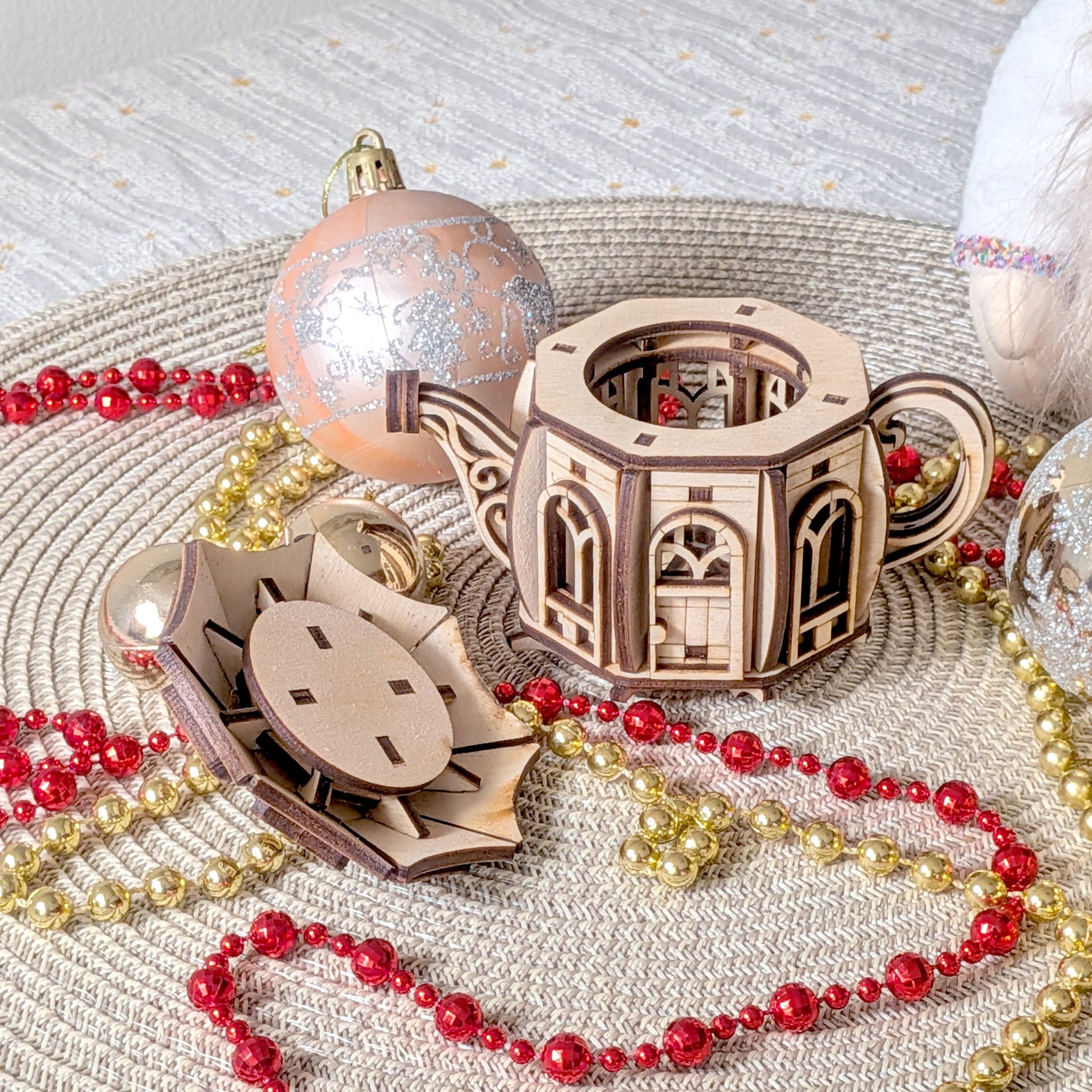 The teapot fairy house with the lid removed, showing the internal laser cut structure, surrounded by Christmas ornaments and festive bead garlands