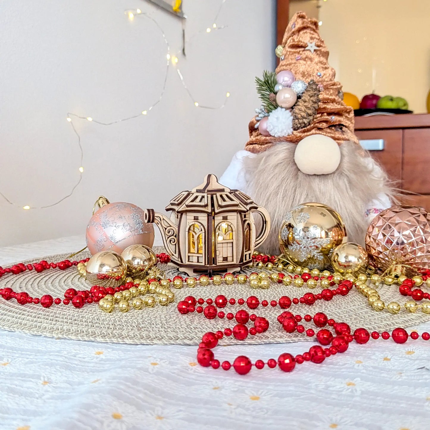 Fairytale teapot house made of laser cut plywood with glowing inner light, staged with a plush Christmas gnome and baubles