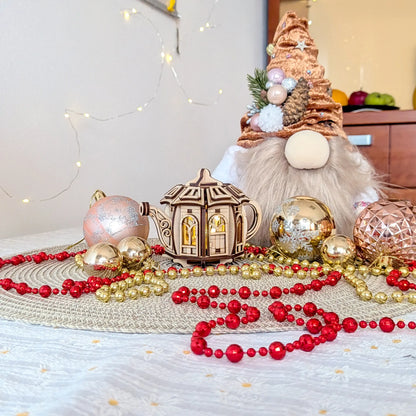 Fairytale teapot house made of laser cut plywood with glowing inner light, staged with a plush Christmas gnome and baubles