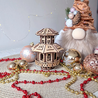 A miniature multi-tier pagoda fairy house of laser cut plywood, beautifully staged with a holiday gnome and gold baubles
