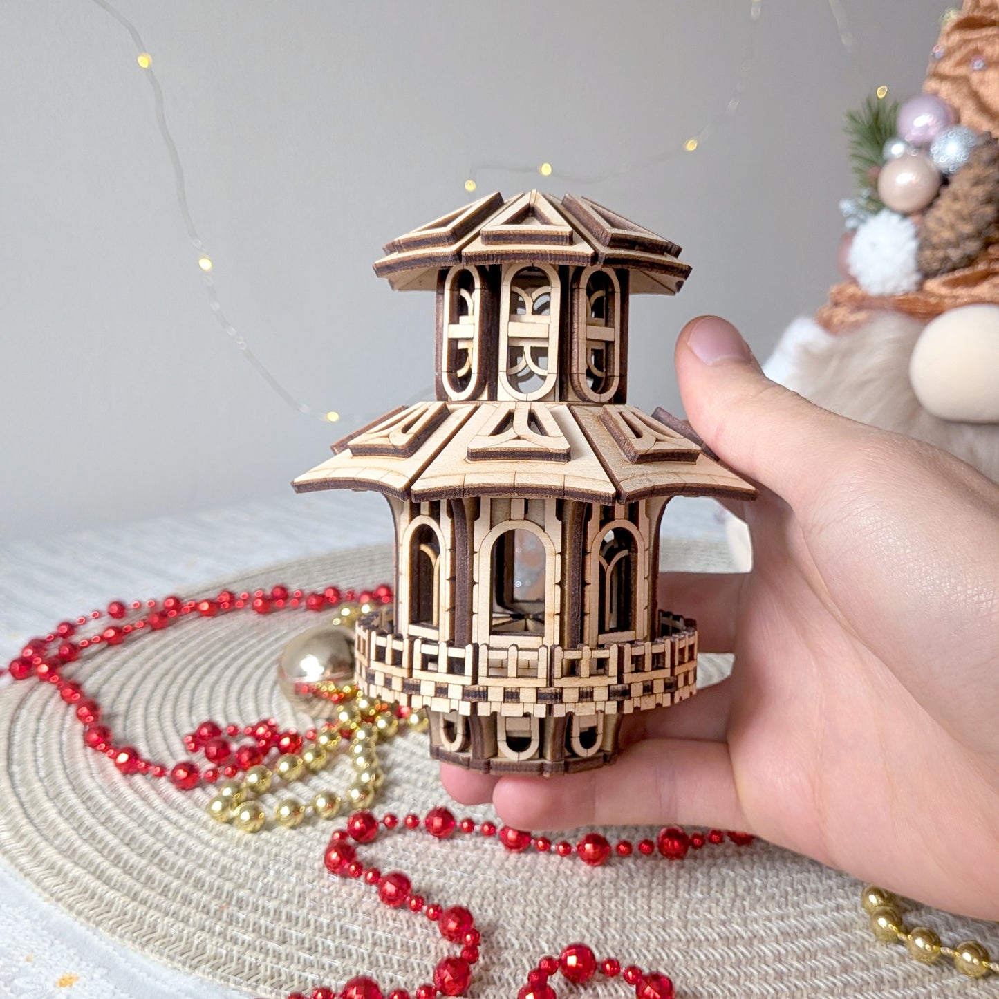 Hand holding a detailed two-level wooden Faelight House miniature with arched windows, placed on a festive table with Christmas ornaments