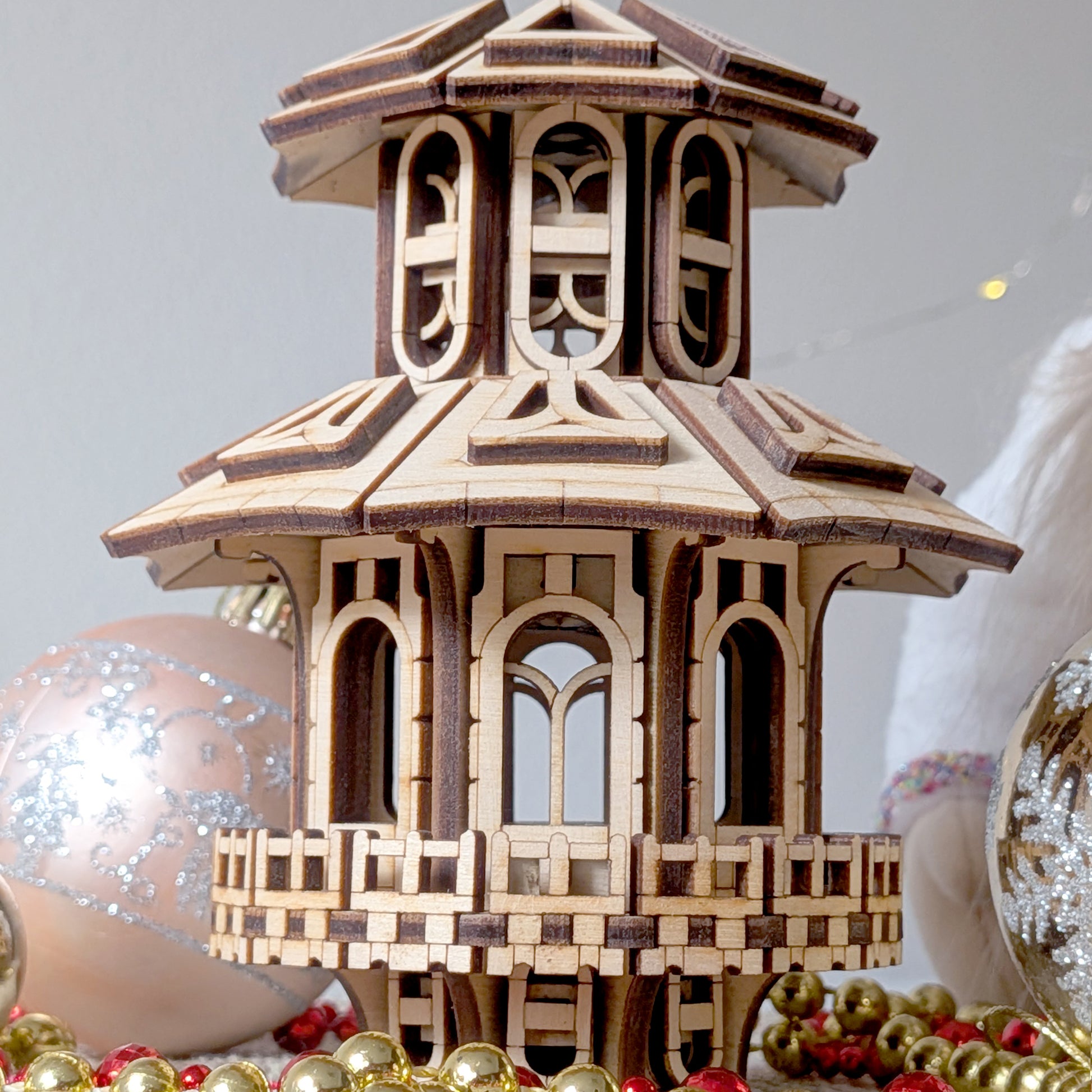 Close-up view of the wooden Faelight House showing intricate laser-cut windows, balcony details, and fine layered roof structure
