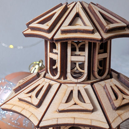 Close-up of the upper roof and tower of the wooden Faelight House, highlighting the geometric layered roof design and decorative window arches