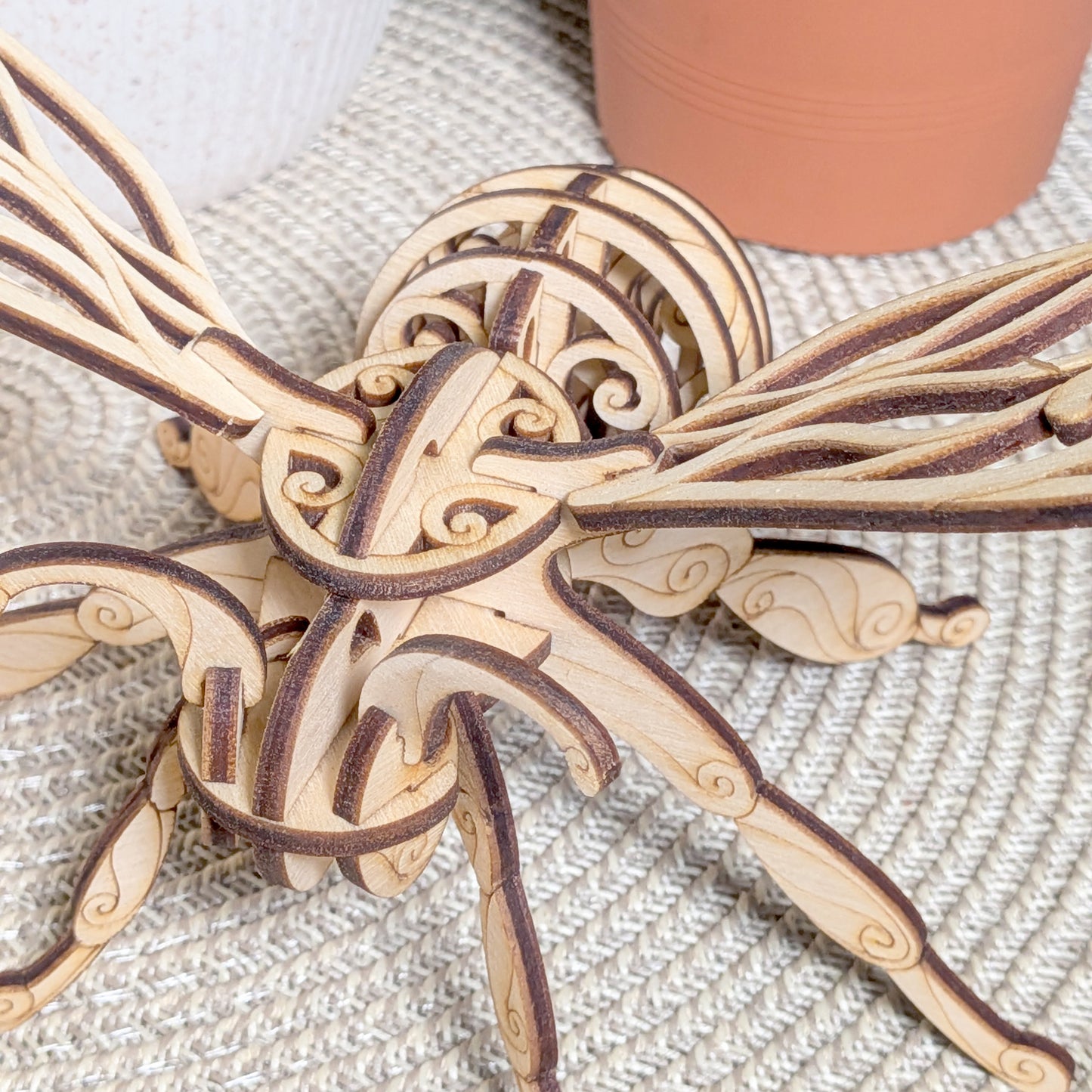Close-up of the laser cut wooden fairy bee ornament, highlighting intricate swirled patterns and layered plywood design