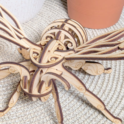 Close-up of the laser cut wooden fairy bee ornament, highlighting intricate swirled patterns and layered plywood design