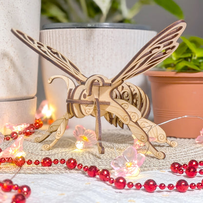 Close-up of laser cut plywood fairy bee ornament with intricate layered wings and floral light decoration, placed near houseplants