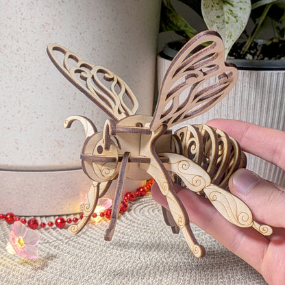 Wooden fairy bee ornament crafted from laser cut plywood, held in hand to show scale and detailed scrollwork on wings and legs