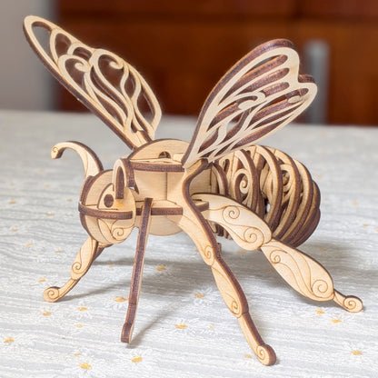 Laser cut wooden fairy bee ornament with elegant layered plywood design, featuring intricate wings and detailed scroll patterns, displayed on a light textured tablecloth