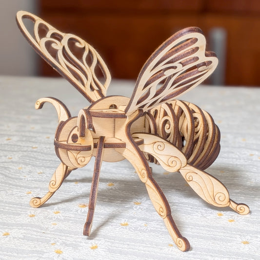 Laser cut wooden fairy bee ornament with elegant layered plywood design, featuring intricate wings and detailed scroll patterns, displayed on a light textured tablecloth