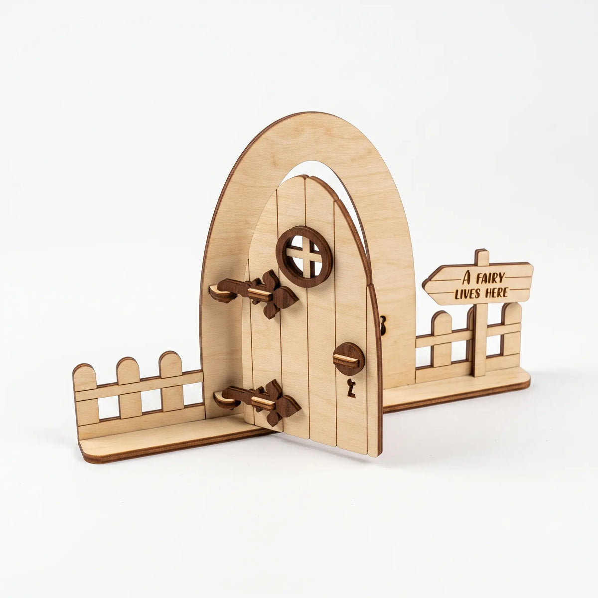 Standing laser cut plywood fairy door with picket fence panels, round window, and a sign reading A fairy lives here.