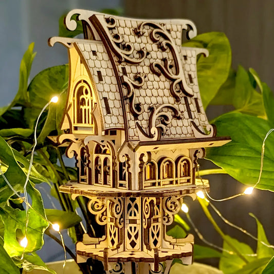 Fairy Elf House Laser cut model of a decorative fantasy house with intricate details, surrounded by green leaves and string lights.