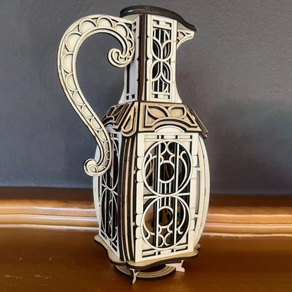 Side view of a physical laser cut plywood jug fairy house showing decorative cutout window patterns and a scrolled handle.