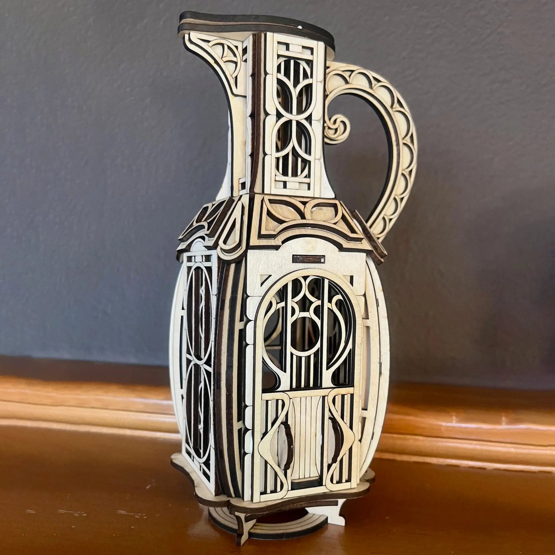 Assembled laser cut plywood jug house featuring a detailed arched front door, standing on a dark wooden mantelpiece shelf.