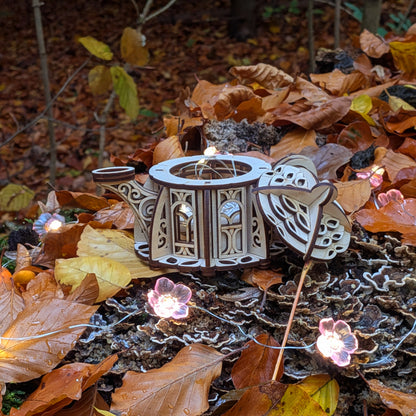 Disassembled laser cut kettle house showing open top and removable lid, photographed on colorful forest leaves.