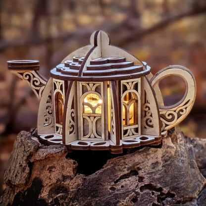 Laser cut fairy kettle house SVG file displayed as a glowing wooden teapot lantern in a forest setting, showing intricate plywood details for DIY crafting