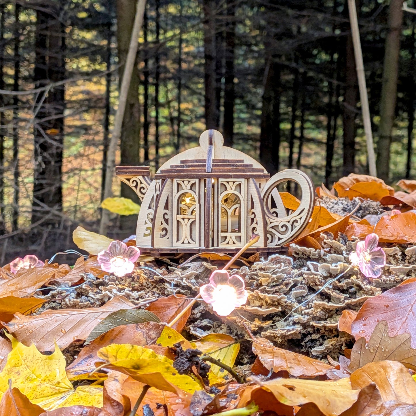 Laser cut wooden kettle house with glowing windows nestled among autumn leaves in a magical forest background