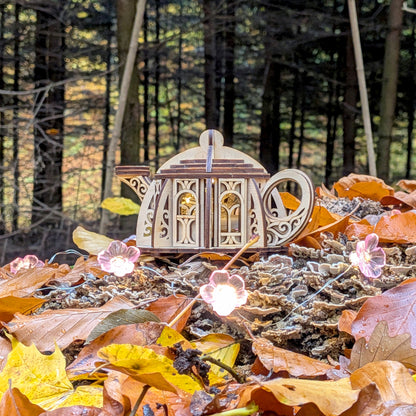 Laser cut wooden kettle house with glowing windows nestled among autumn leaves in a magical forest background