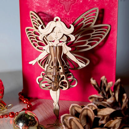 3D laser cut plywood fairy ornament placed on a festive holiday table with gold baubles, red beads, and pinecone decor.