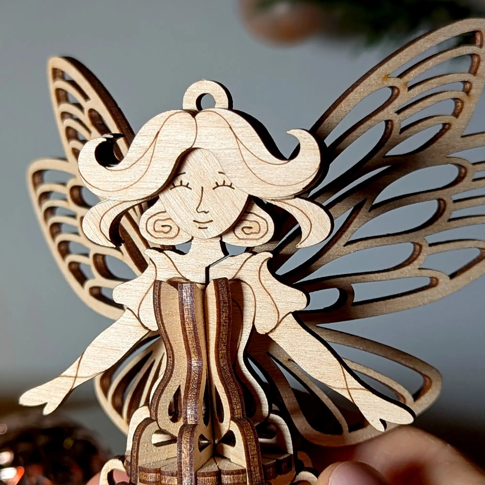 Close-up portrait of an elegant 3D laser cut plywood fairy ornament showing delicate face engraving and wing structure.