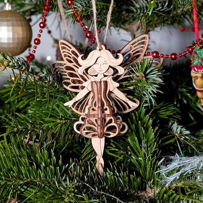 Close-up of a 3D laser cut plywood fairy ornament with ornate wings hanging on a lush green Christmas tree with lighting.
