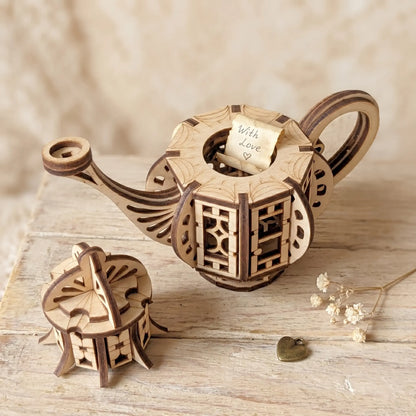 Teapot fairy house laser cut file with opening lid and tiny hidden space, shown on a rustic wooden surface with a small note, charm, and dried flowers.