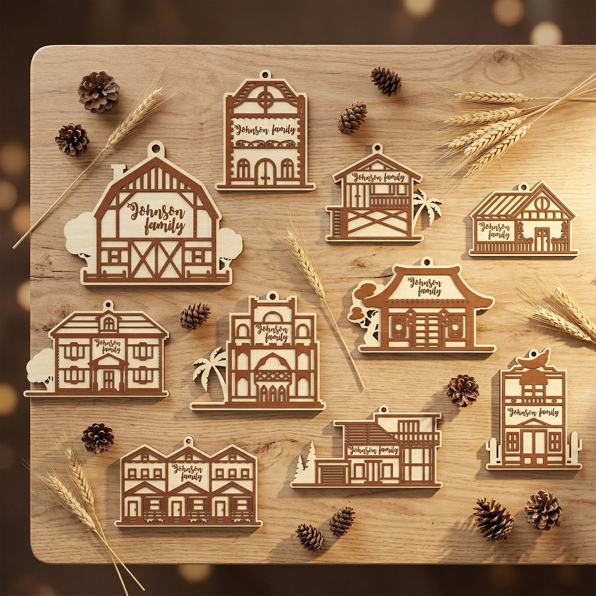 A variety of custom house-shaped ornaments crafted from laser-cut plywood in different architectural styles. Each ornament features the engraved text "Johnson family." Arranged on a wooden table with rustic decor like pine cones and wheat stalks to showcase personalized gift options.