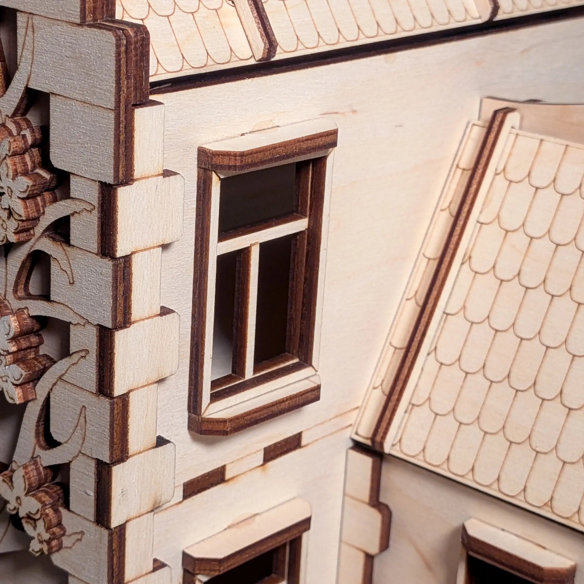 Close-up of a window, shingle tiled roof, and a beautifully engraved blooming tree on a laser cut plywood dollhouse wall