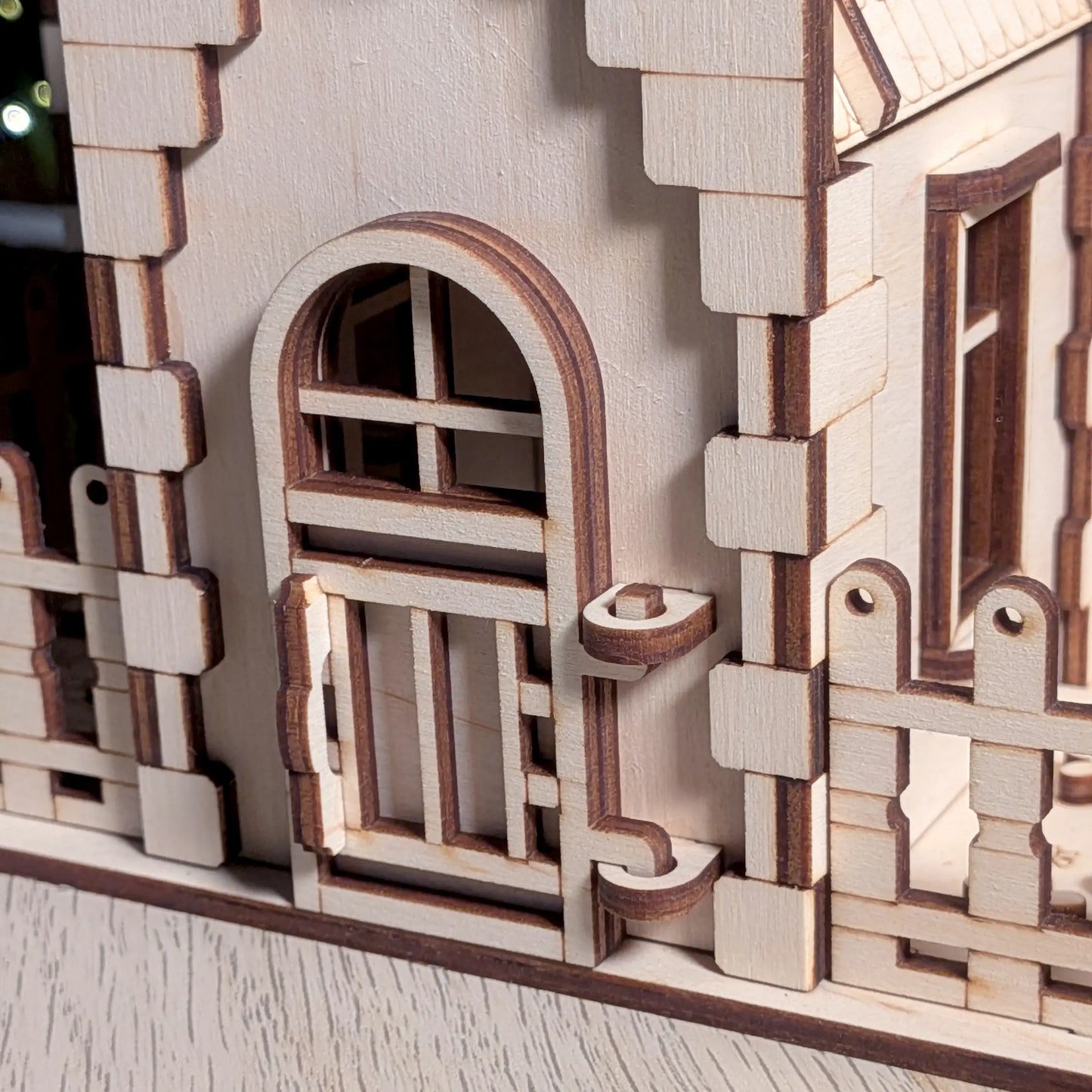 Close-up of an arched entryway door, a tiny latch, and layered brick textures on a laser cut plywood miniature dollhouse