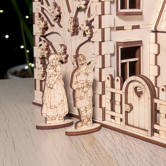 Two small wooden figurines of a man and a woman standing next to a heart gate of a detailed laser cut plywood family house.