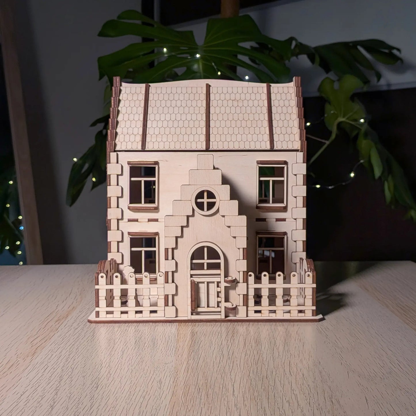 Front view of a two-story laser cut plywood family dollhouse kit featuring a small picket fence and a gabled entry door.
