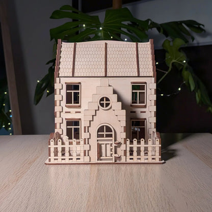 Front view of a two-story laser cut plywood family dollhouse kit featuring a small picket fence and a gabled entry door.