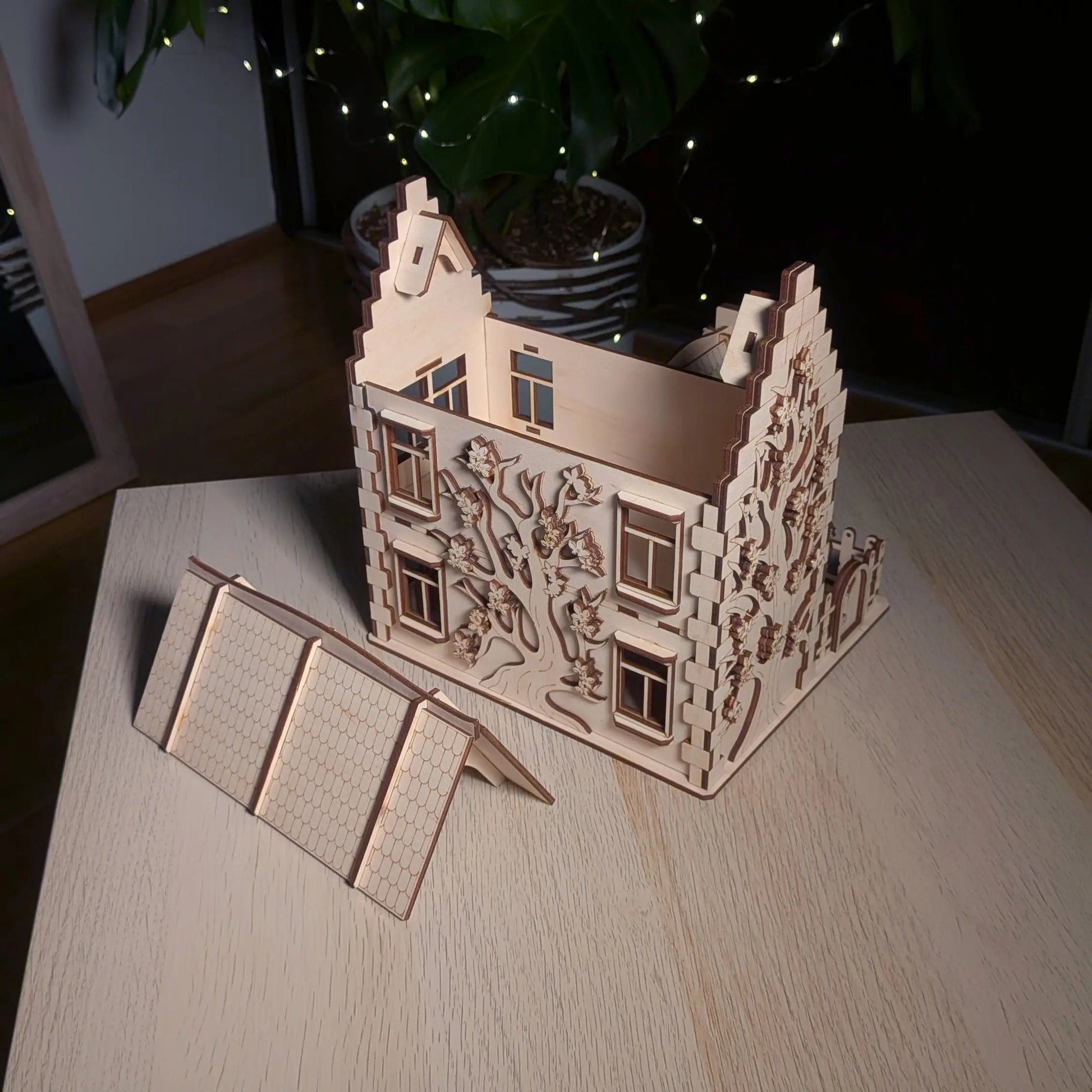 High angle view showing a removable roof panel next to the main body of an engraved laser cut plywood family dollhouse.