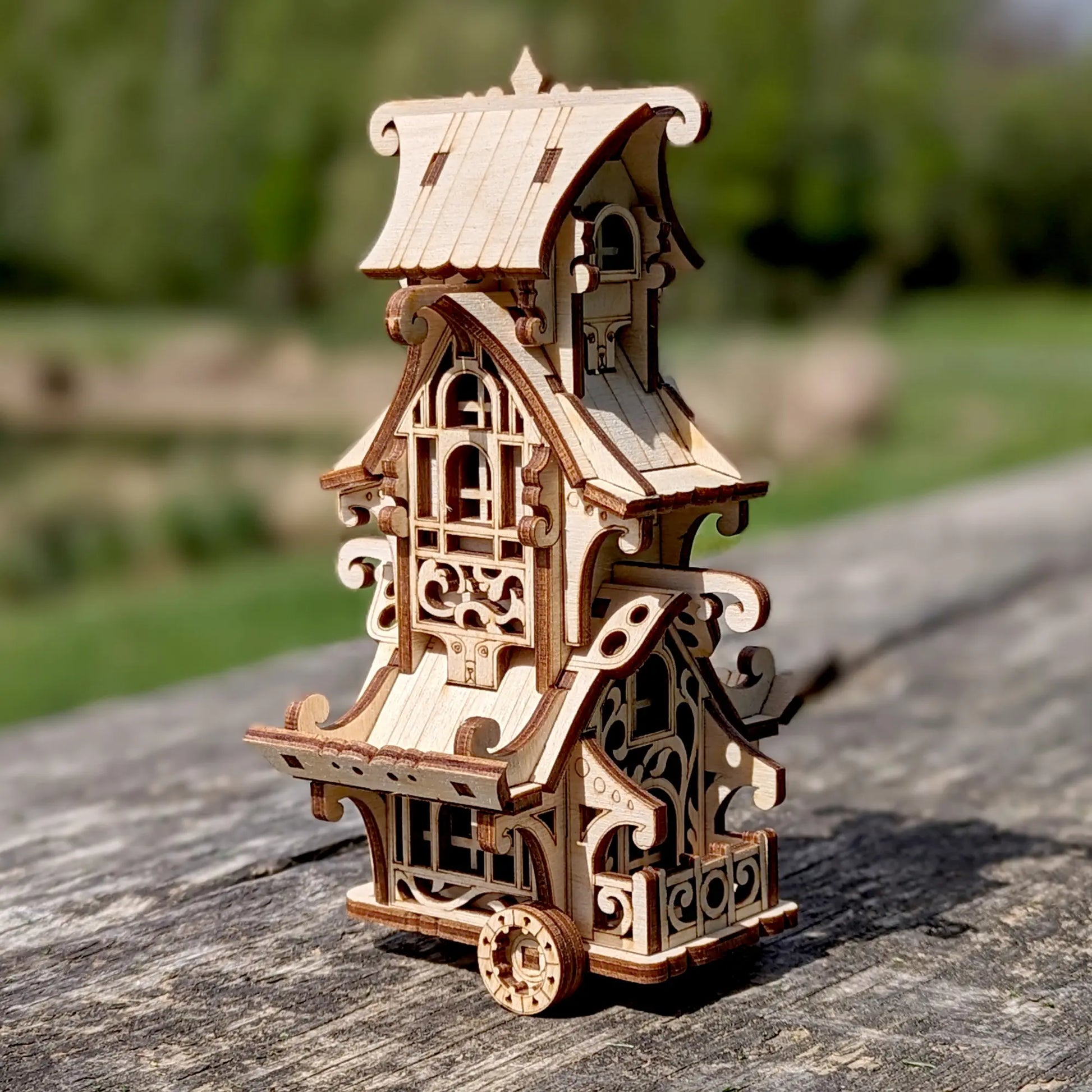 Wide shot of a whimsical laser cut plywood mobile home miniature positioned next to giant old tree roots in woods.