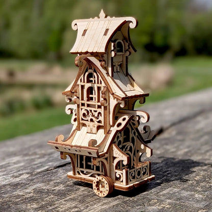 Wide shot of a whimsical laser cut plywood mobile home miniature positioned next to giant old tree roots in woods.