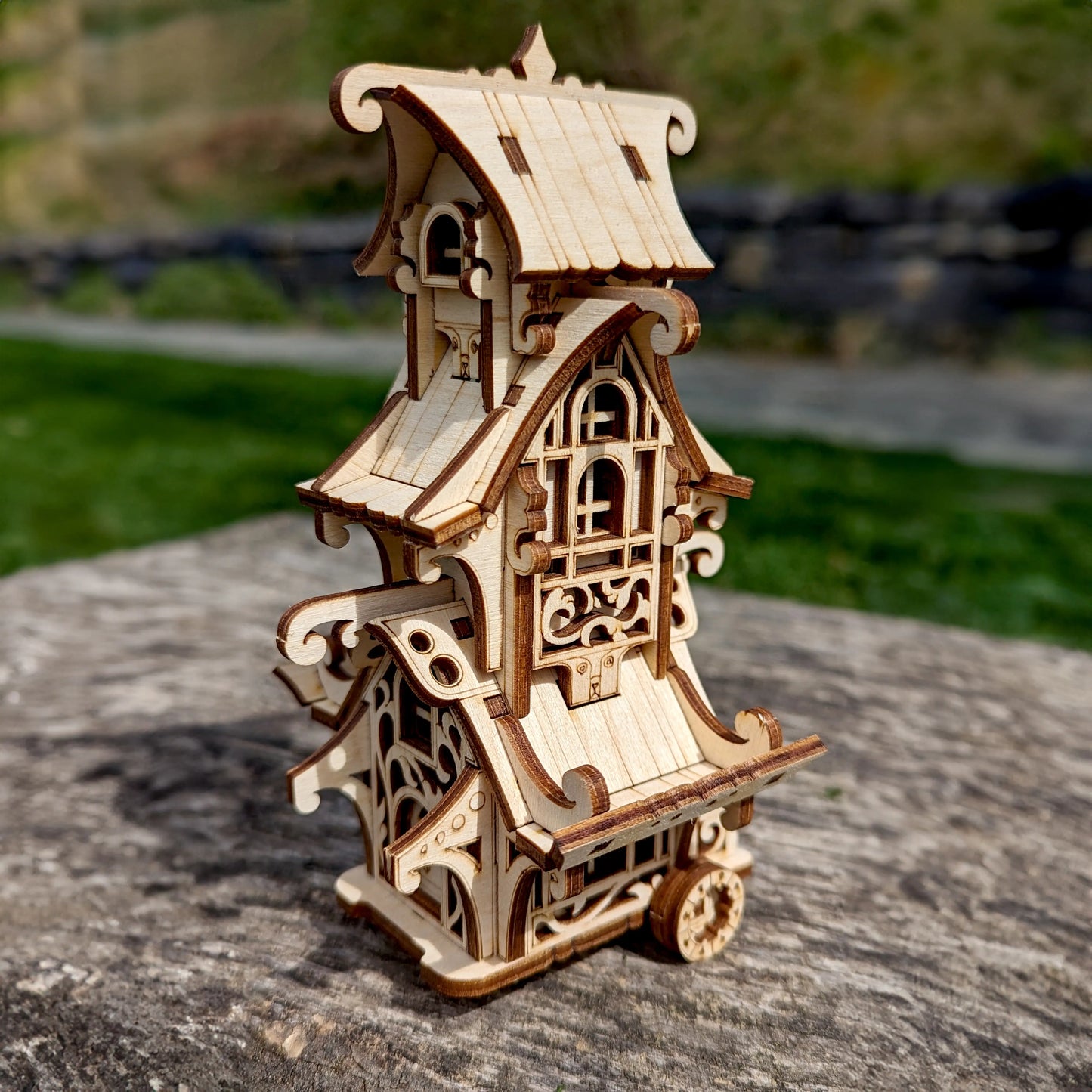 Side perspective view of a mini fantasy travel trailer puzzle made of laser cut plywood, staged on a big stone.