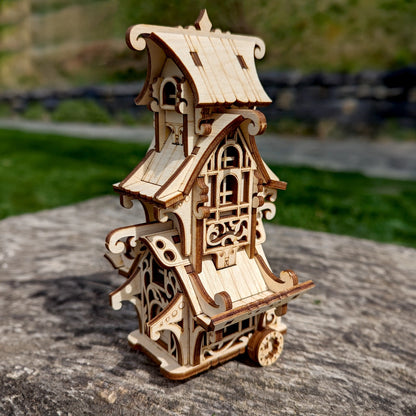 Side perspective view of a mini fantasy travel trailer puzzle made of laser cut plywood, staged on a big stone.