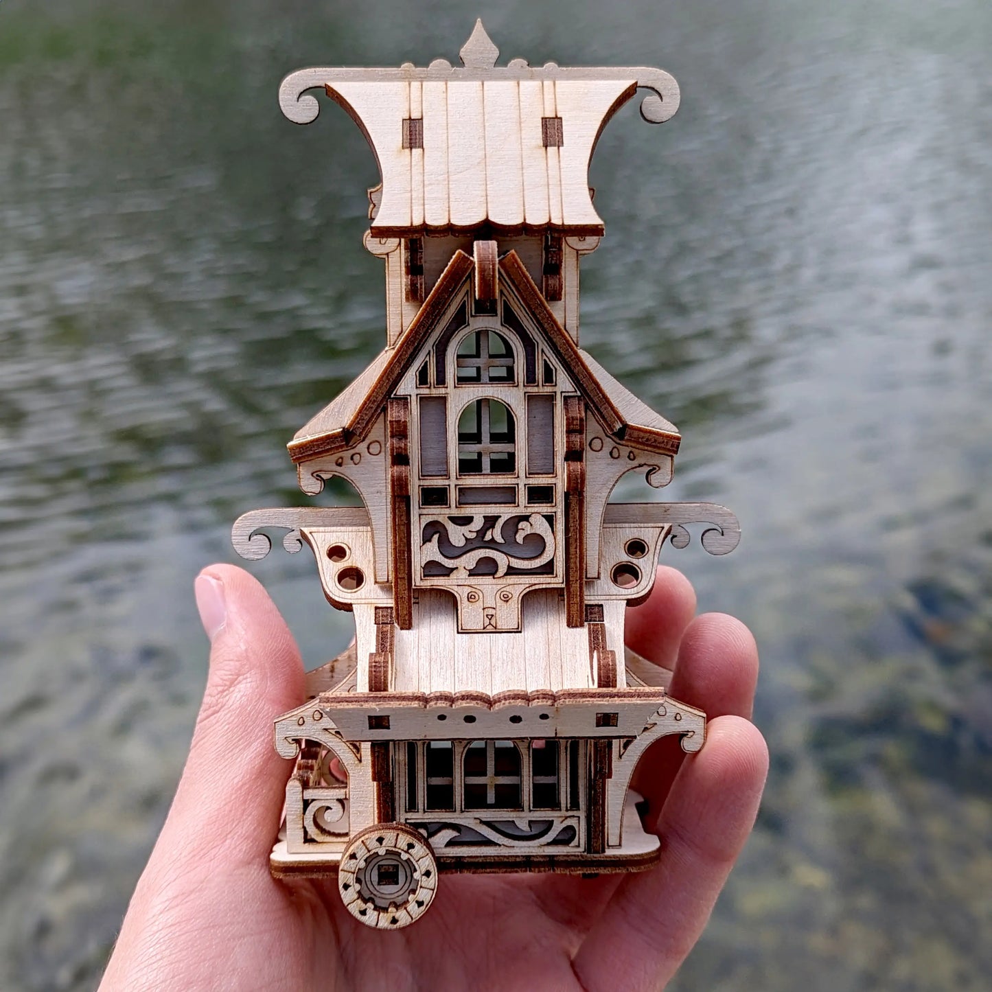 Rear-facing perspective of an assembled laser cut plywood vintage caravan toy displayed outdoors on a mossy rock.