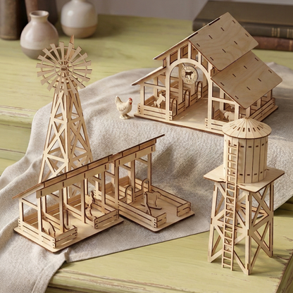Wooden laser cut model of a farm scene with a windmill and barn on a table.