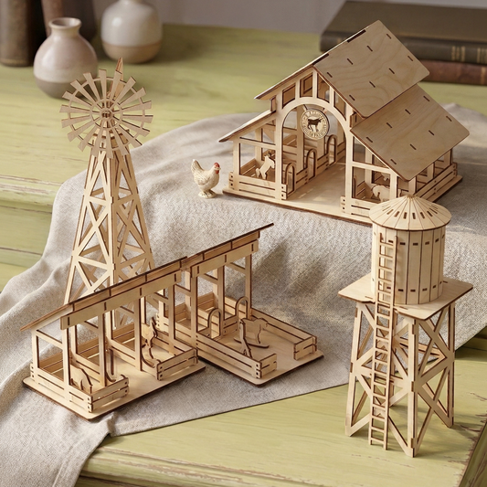 Wooden laser cut model of a farm scene with a windmill and barn on a table.