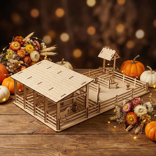 High-angle view of a laser cut plywood farm set featuring a large stable with a detailed shingle-pattern roof. The toy sits on a wooden table surrounded by mini pumpkins, dried flowers, and fairy lights, showing its scale as a tabletop playset.