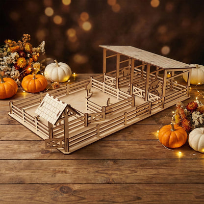 Side view of the wooden farm yard made from light-colored plywood. Focus is on the fenced enclosure and a small gabled gatehouse. The intricate laser-cut joints are visible. White and orange pumpkins are placed around the toy on a rustic table