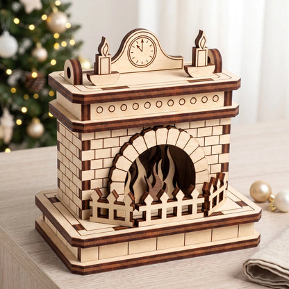 Unfinished laser cut plywood fireplace model on wooden tabletop next to illuminated Christmas tree and golden ornaments.