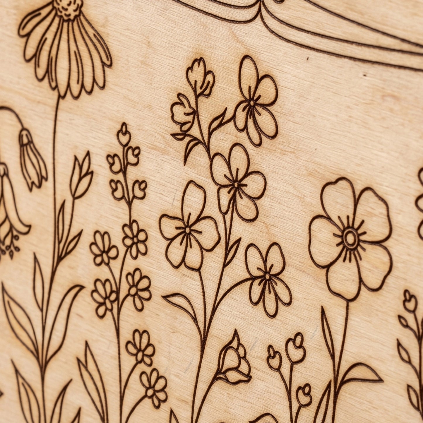Close-up macro detail of an intricate wildflower engraving on a laser cut plywood surface.