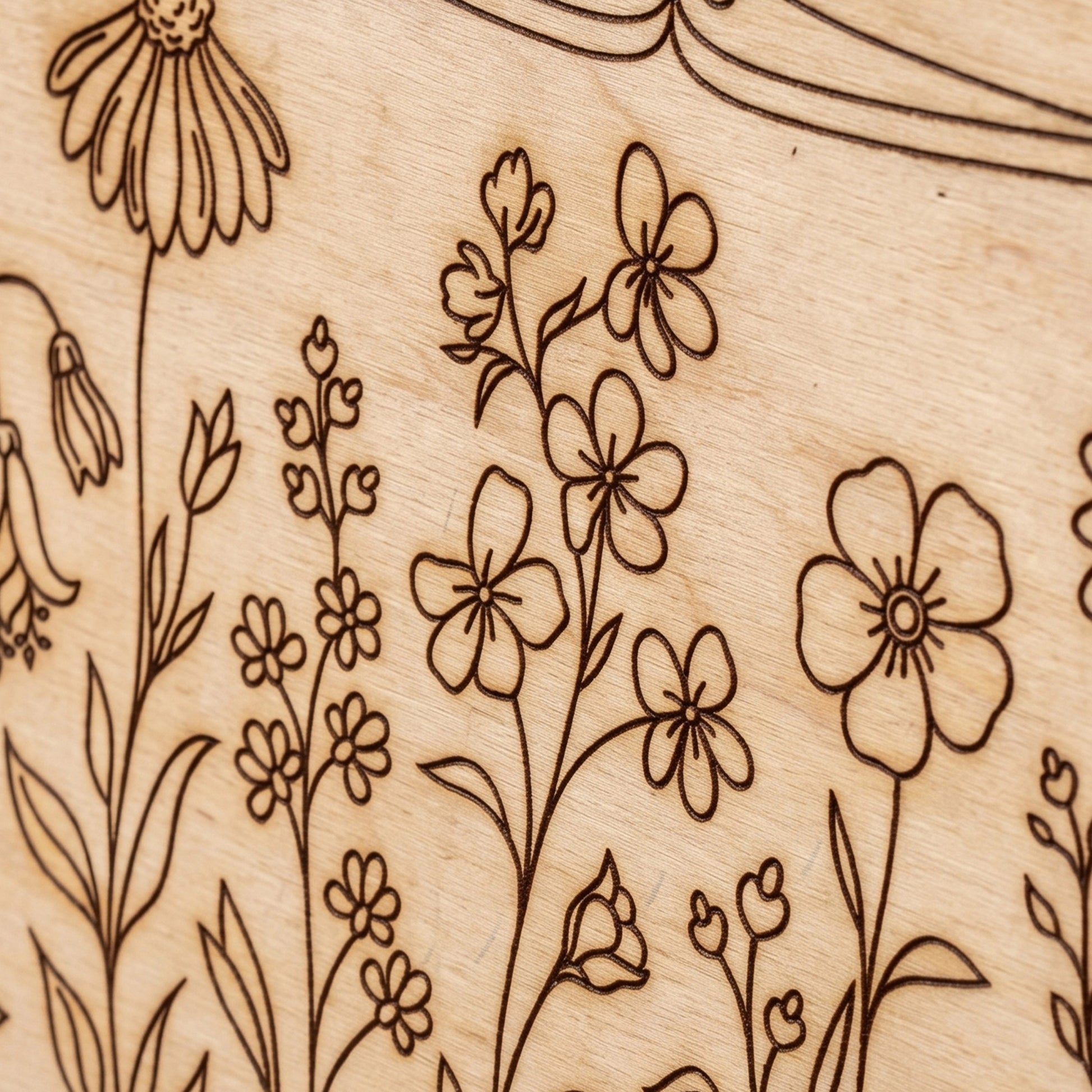 Close-up macro detail of an intricate wildflower engraving on a laser cut plywood surface.