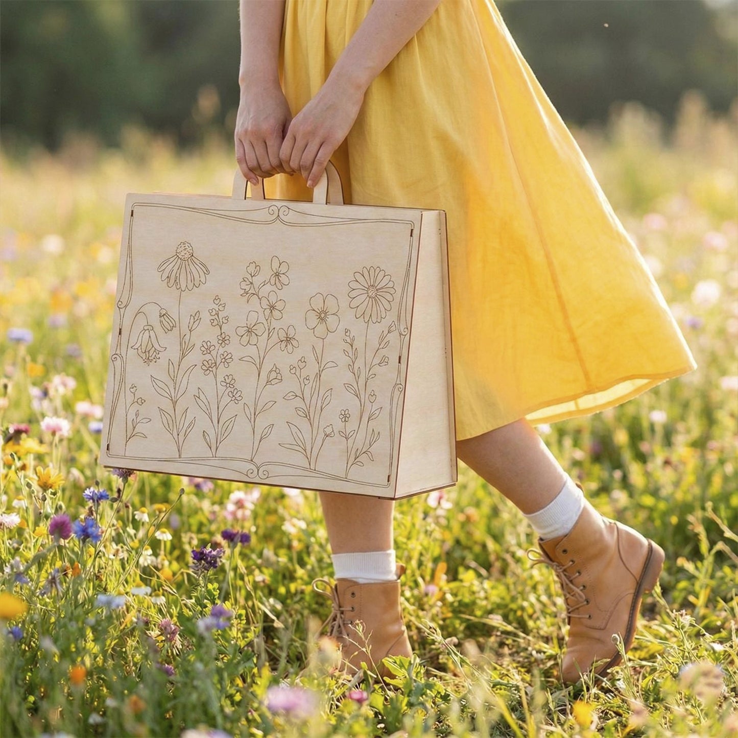 A woman in a yellow dress and boots is walking through a field of colorful wildflowers, holding a laser cut plywood floral gift bag