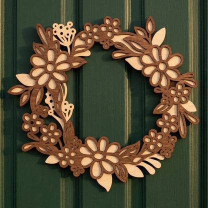 Frontal view of a 3D layered laser-cut wooden spring wreath featuring a floral daisy design. The wreath is composed of two contrasting plywood layers—a light wood base and a dark brown wood-stained overlay. Displayed centered on a green paneled door, showcasing the precise cutouts and modern rustic style.