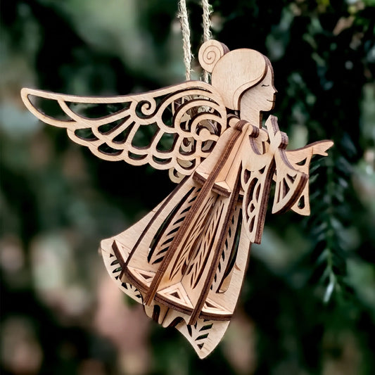 3D laser cut plywood flying angel ornament with trumpet and filigree wings hanging by twine among outdoor pine branches.